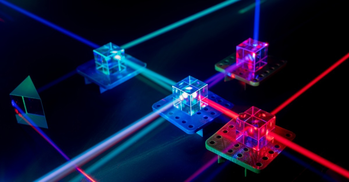 A purple laser beam crosses a glass plate and optical mounts on a perforated laboratory table with green light.