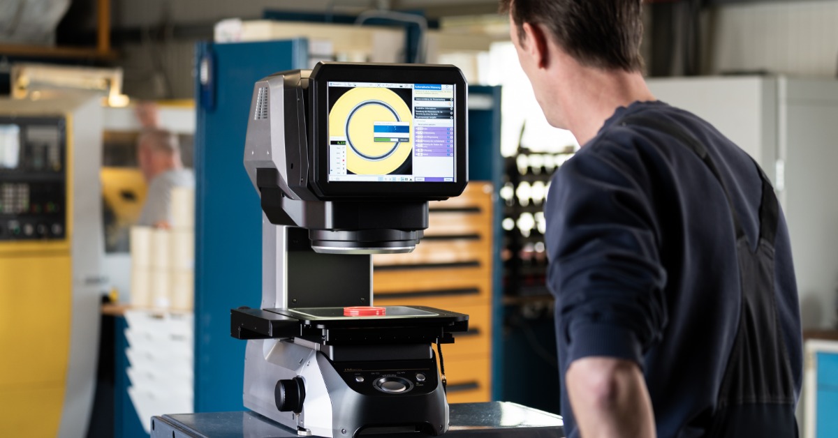 A technician inspects a small part on a digital measuring machine in a precision manufacturing shop.